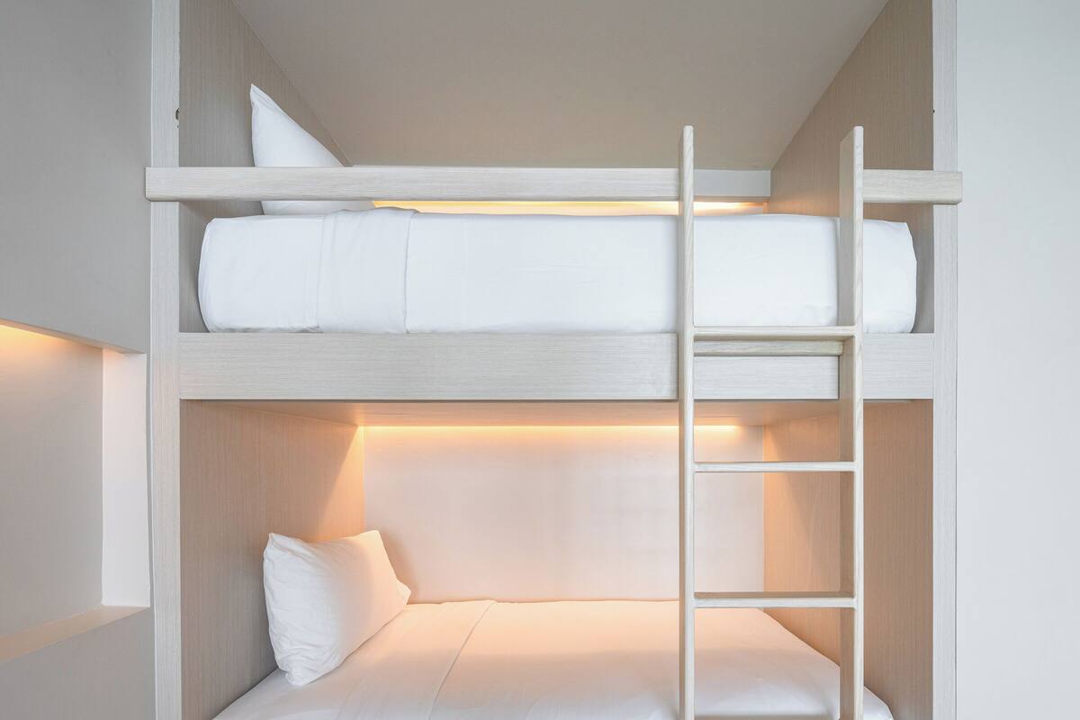 A bunk bed with a ladder, white bedding, and a light-colored wall.