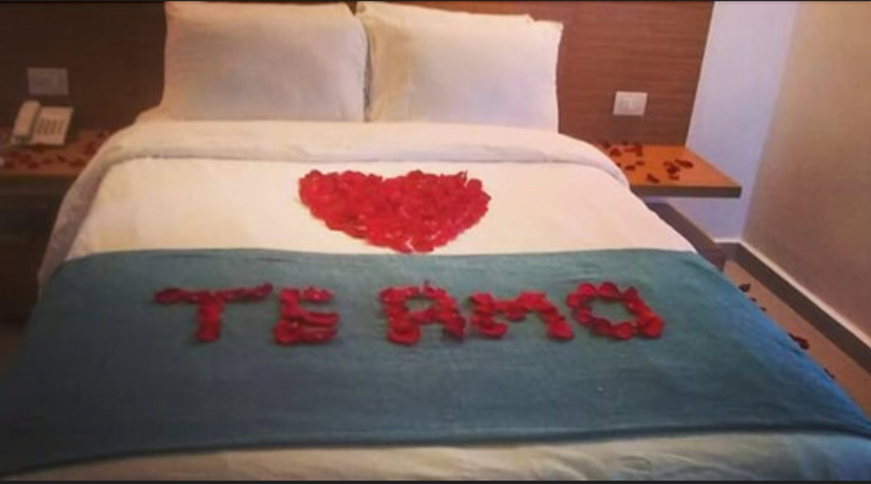Una cama con un adorno con forma de corazón y la frase 'TE AMO' en la colcha.
