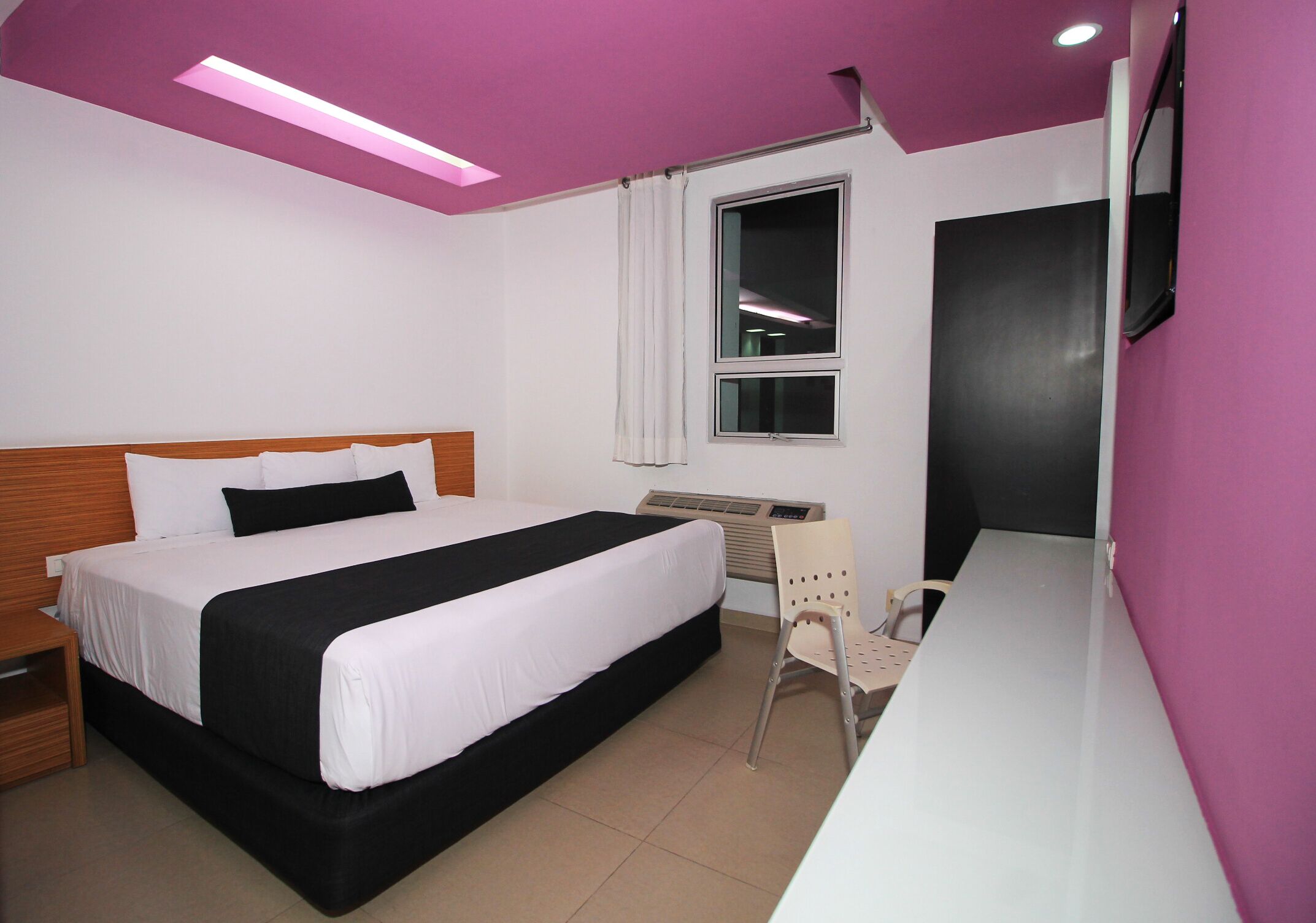 A hotel room with a bed, a desk, a chair, and a window.