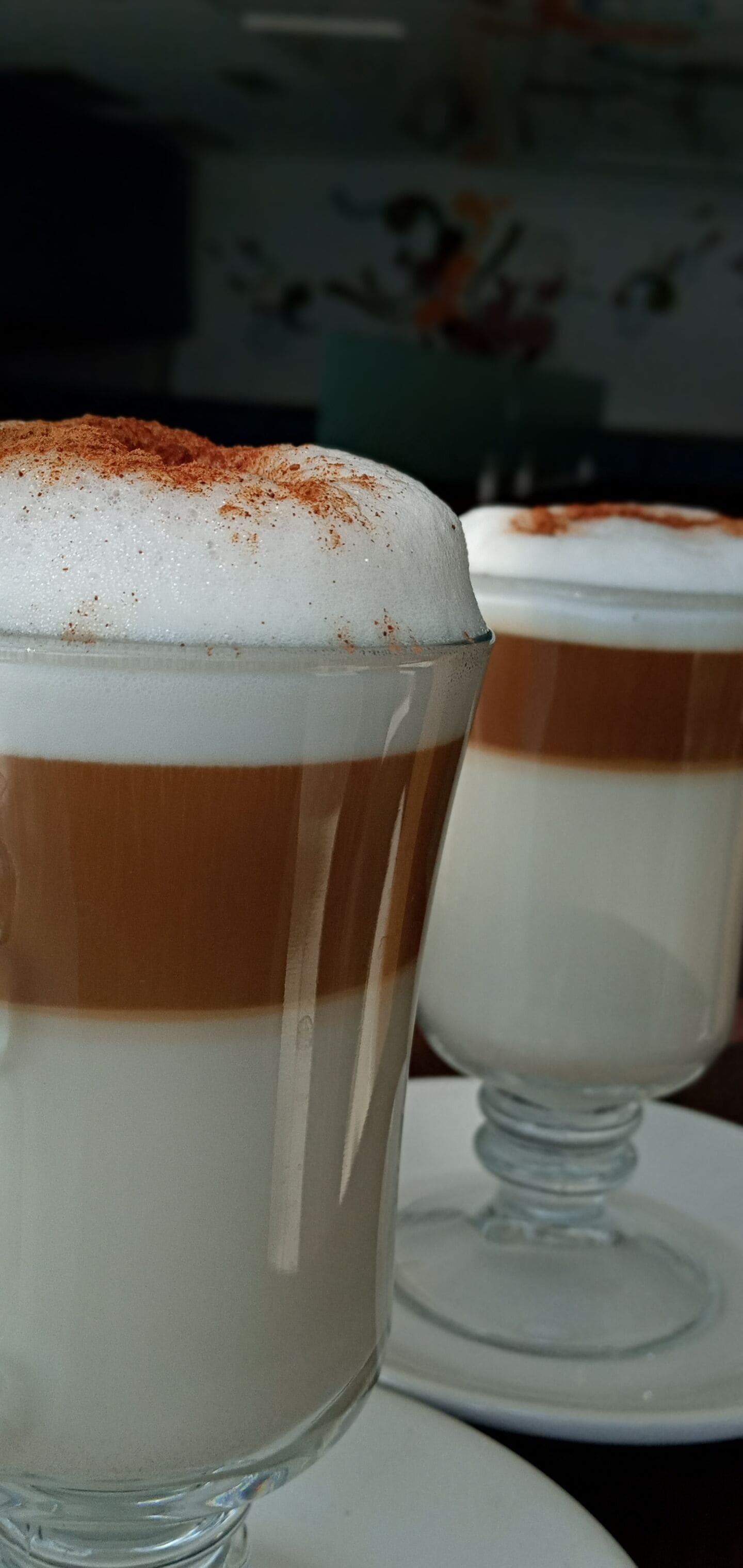 Zwei Gläser mit mehrschichtigen Desserts mit schaumiger Oberfläche, platziert auf weißen Tellern.