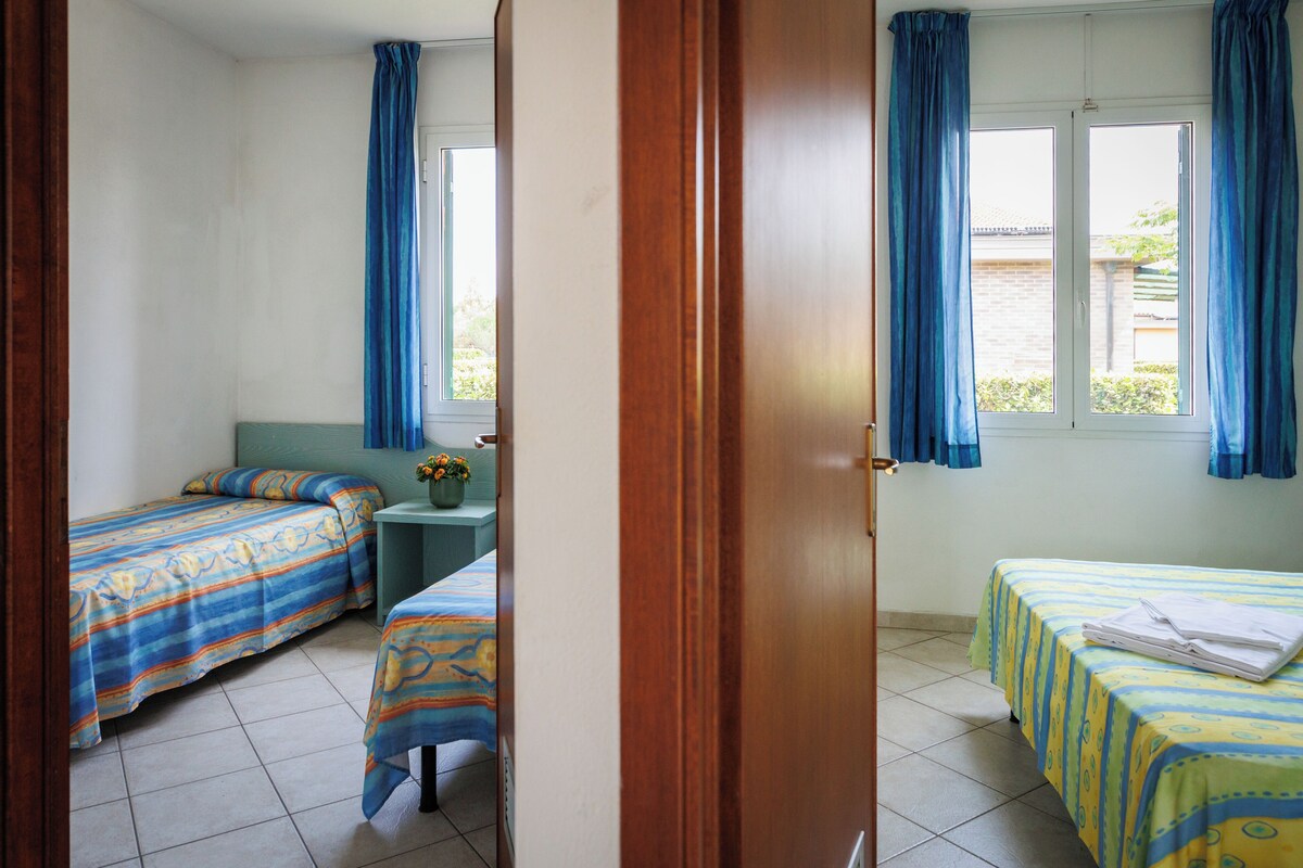 A room with two beds, a small table with a vase, and a window with curtains.