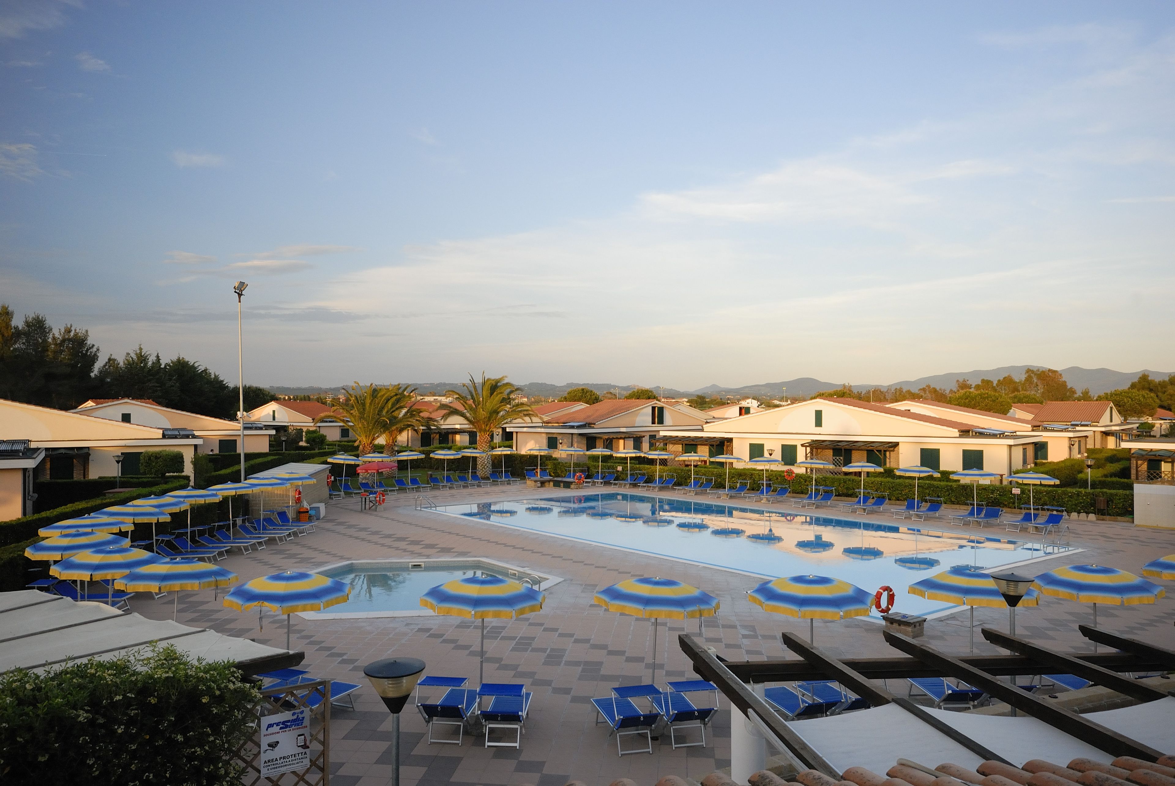 Un área de piscina con múltiples sillas de descanso y sombrillas, rodeada de edificios con un estilo arquitectónico uniforme.