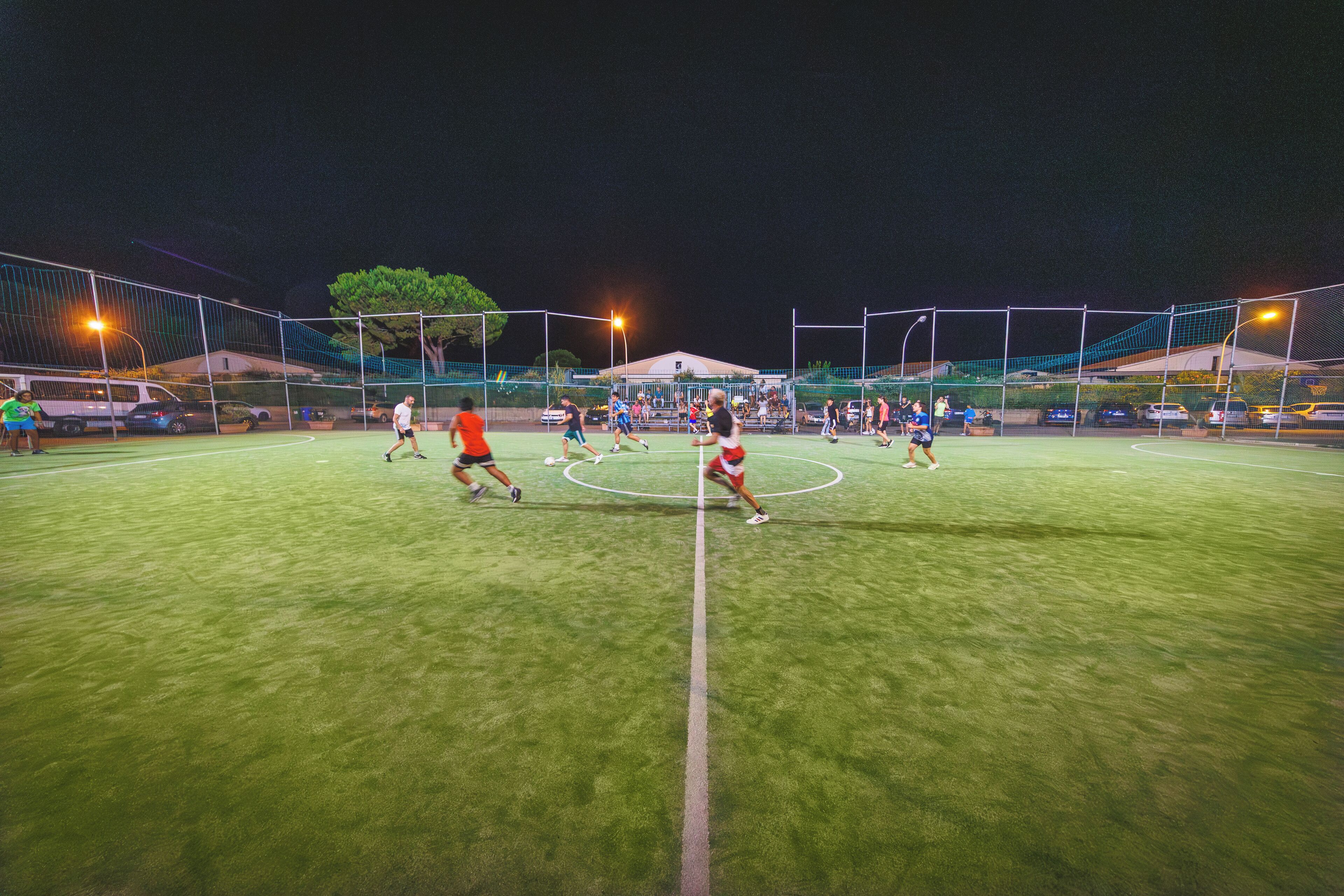 Ein Fußballfeld bei Nacht mit Tor, Flutlicht und einem Netz umzäunt.