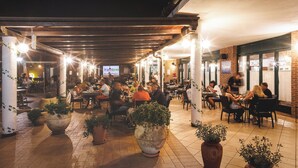 An outdoor dining area with multiple tables and chairs, potted plants, and a covered roof structure. - La Cecinella (Cecina)