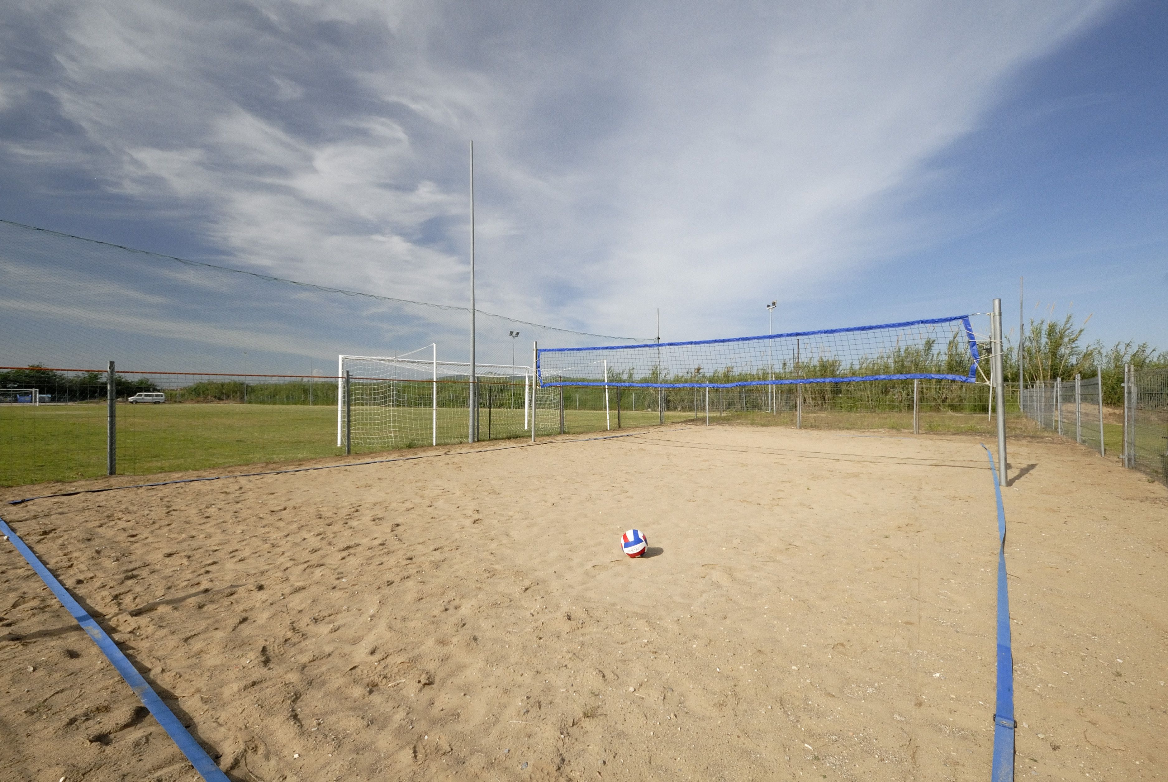 Una spiaggia con un campo da pallavolo sabbioso, una rete, una recinzione e alberi.