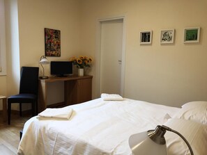 Habitación de hotel con una cama, un escritorio con computadora, una silla, una lámpara y una puerta.