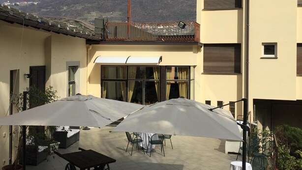 A building with a patio area featuring outdoor furniture and umbrellas, overlooking a mountainous landscape. - Trieste (Morbegno)