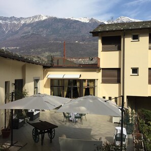 Edificio con un patio amoblado con mobiliario exterior y sombrillas, con vista a un paisaje montañoso.