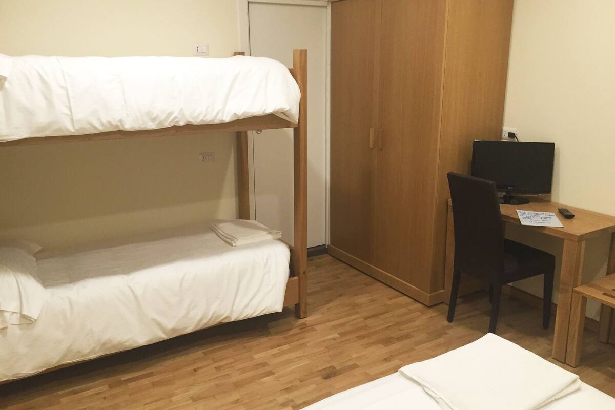 Une chambre de dortoir avec un lit superposé, une armoire en bois, un bureau avec un ordinateur et une chaise.