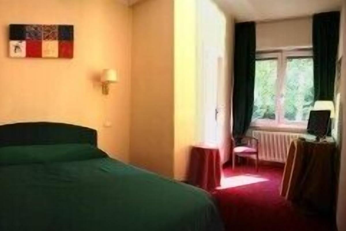 Une chambre d’hôtel avec un lit, deux lampes fixées au mur, une fenêtre avec des rideaux et une petite table avec une chaise.