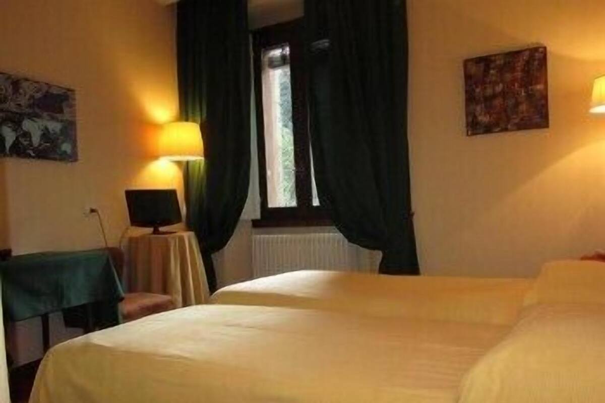 Une chambre d’hôtel avec deux lits, une petite table avec une lampe, une chaise et une fenêtre avec des rideaux.