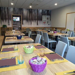 Un restaurante con varias mesas, cada una dispuesta con cubiertos, servilletas y cestas de pan.