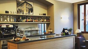 A bar area with a counter, shelves of liquor bottles, coffee machines, and a coffee station. - Trieste (Morbegno)
