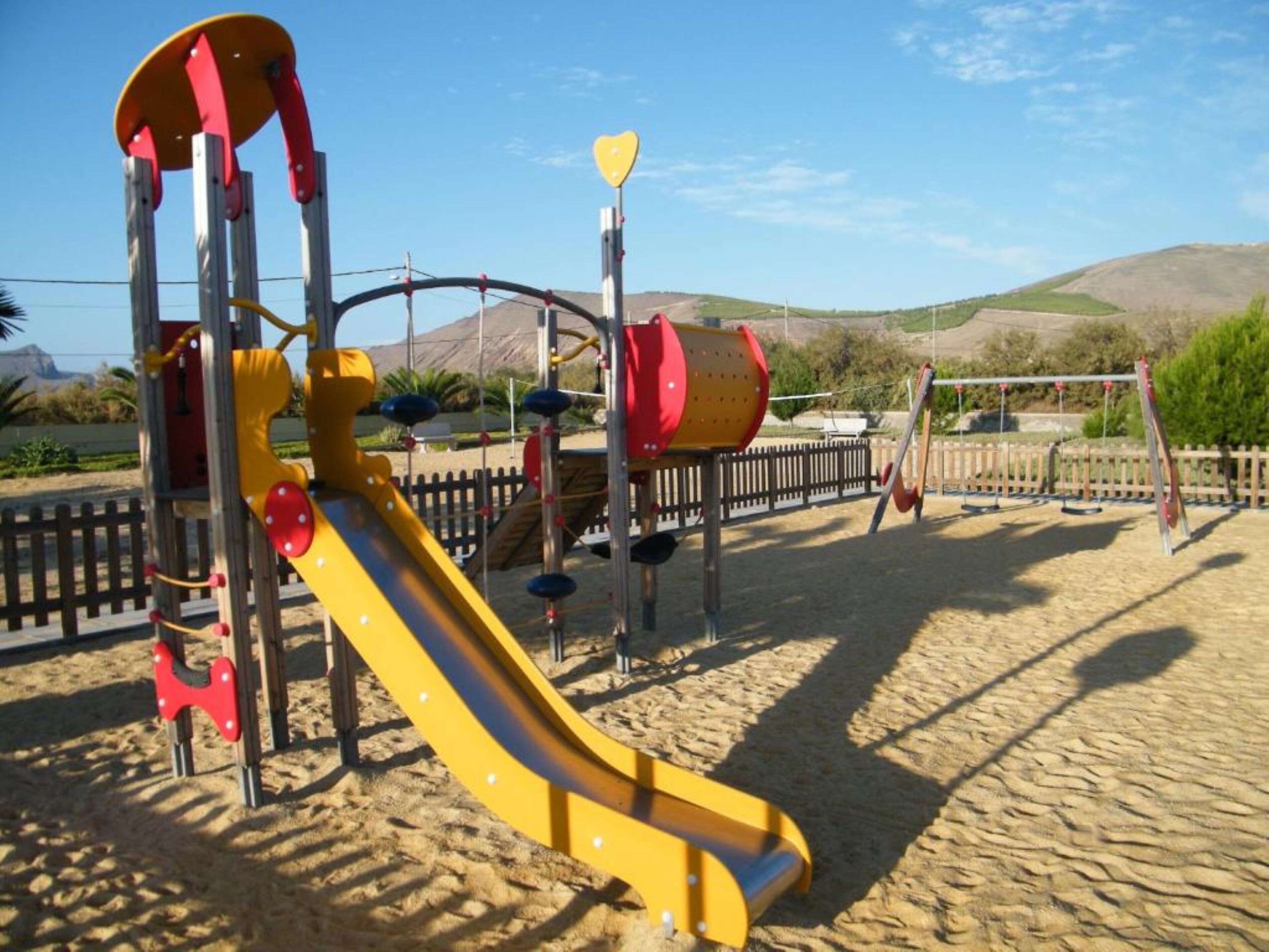 A playground with a yellow slide, climbing structures, and swings.