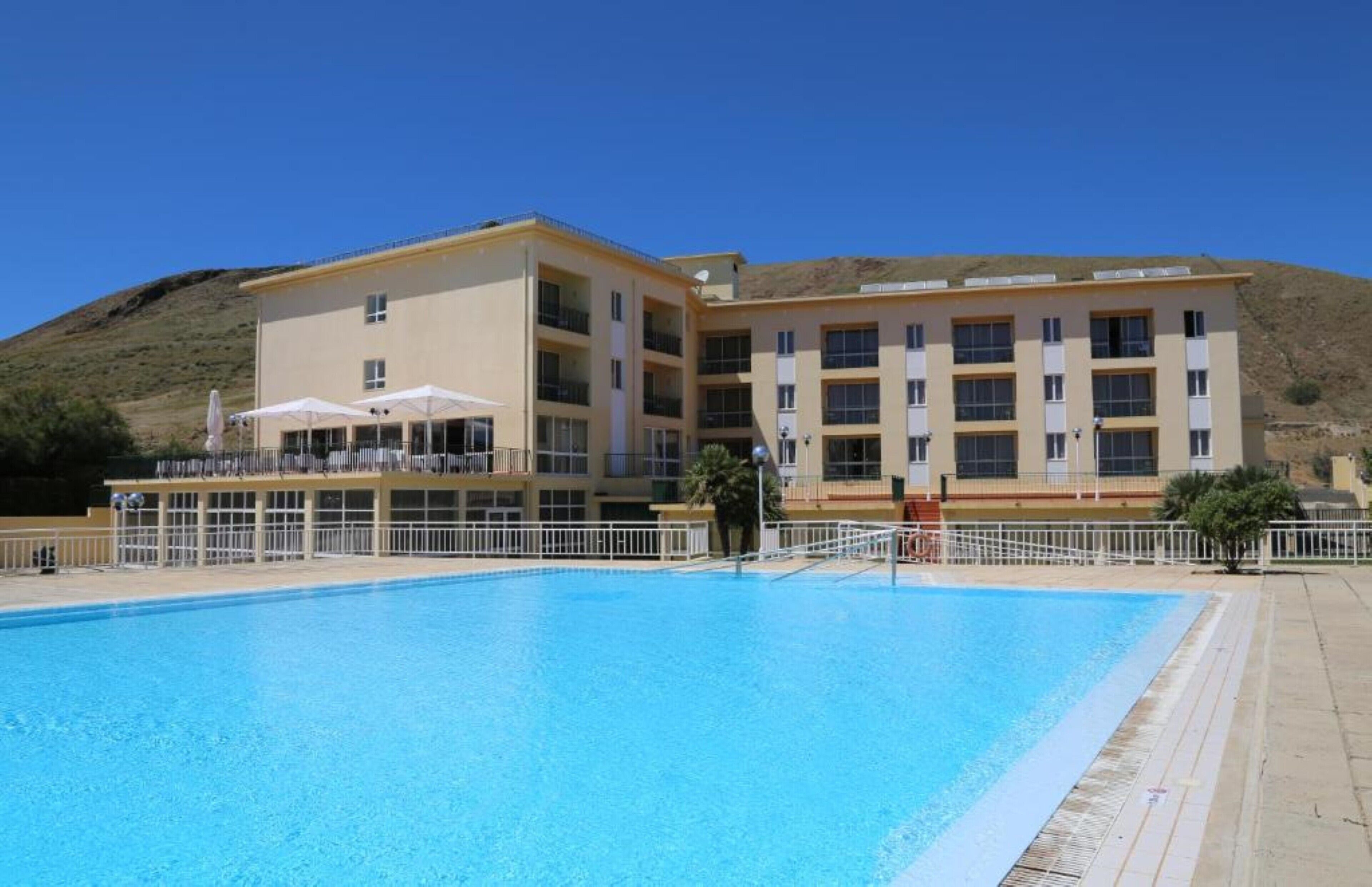 Un albergo con piscina, diversi balconi e tetto piano.