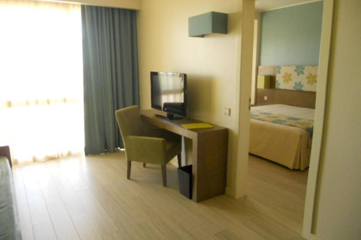 Een hotelkamer met een bed, een bureau met een computer, een stoel en een raam met gordijnen.