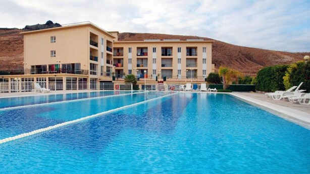 A swimming pool with a building in the background. - INATEL Porto Santo Hotel (Porto Santo)