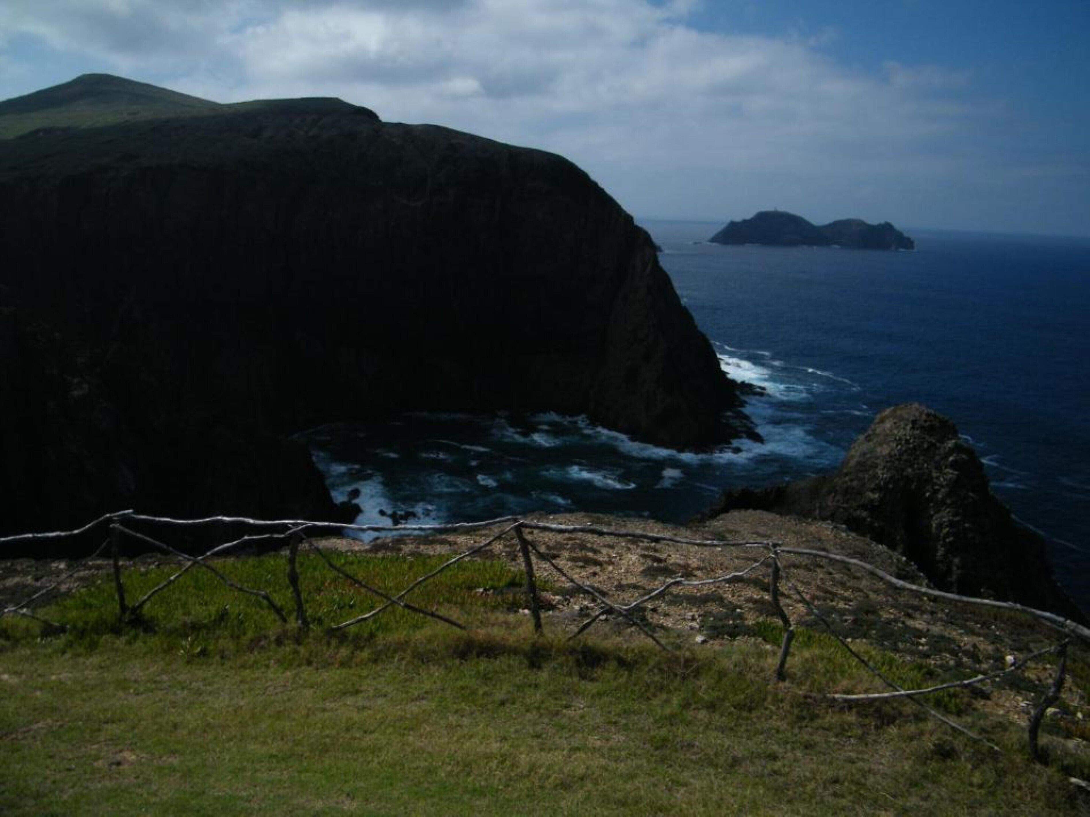 Paisaje costero con un acantilado destacado y una zona cercada al frente.