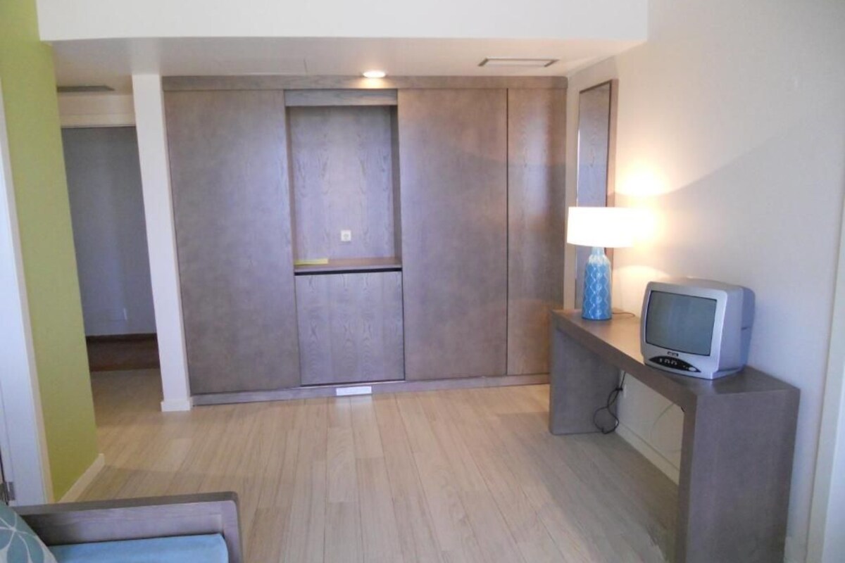 Een hotelkamer met een bed, een bureau met lamp, een televisie en een kledingkast.