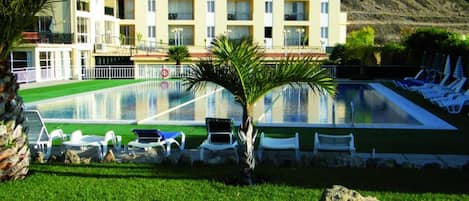 Un hotel con piscina, sillones de descanso y montañas al fondo.