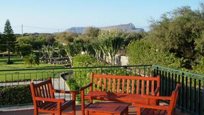 A terrace with a wooden bench and table, surrounded by a green railing, overlooking a landscaped garden and distant mountains. - INATEL Porto Santo Hotel (Porto Santo)