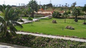 A well-maintained garden with palm trees, a pathway, and a fenced area with a playground. - INATEL Porto Santo Hotel (Porto Santo)