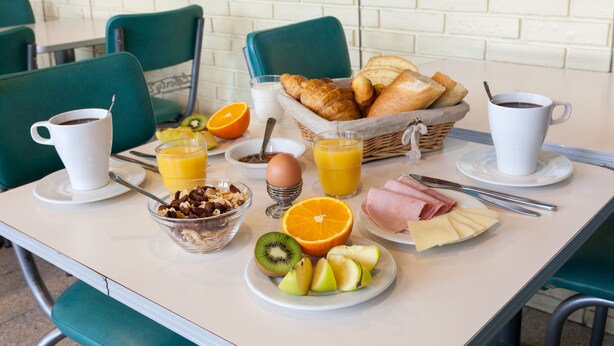 Una mesa de desayuno con cruasanes, jugo de naranja, café y diversas frutas y quesos.