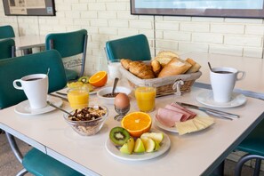Aamiaispöytä, jolla on tarjolla croissantteja, appelsiinimehua, kahvia sekä erilaisia hedelmiä ja juustoja.
