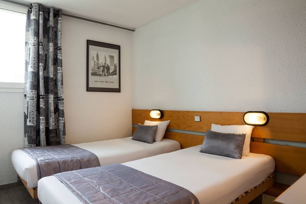 Een hotelkamer met twee eenpersoonsbedden, een lijst aan de muur en een raam met gordijnen.