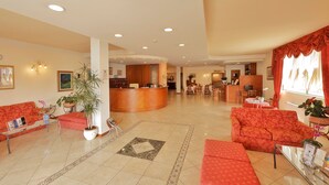 A hotel lobby with a reception desk, seating areas, and a dining area. - Hotel Michelangelo (Terranuova Bracciolini)