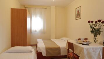 Quarto de hotel com duas camas, uma mesa de jantar com itens de café da manhã, um vaso com flores e um quadro na parede.