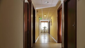 A hotel hallway with a polished floor, wooden doors, and a green exit sign. - Hotel Michelangelo (Terranuova Bracciolini)