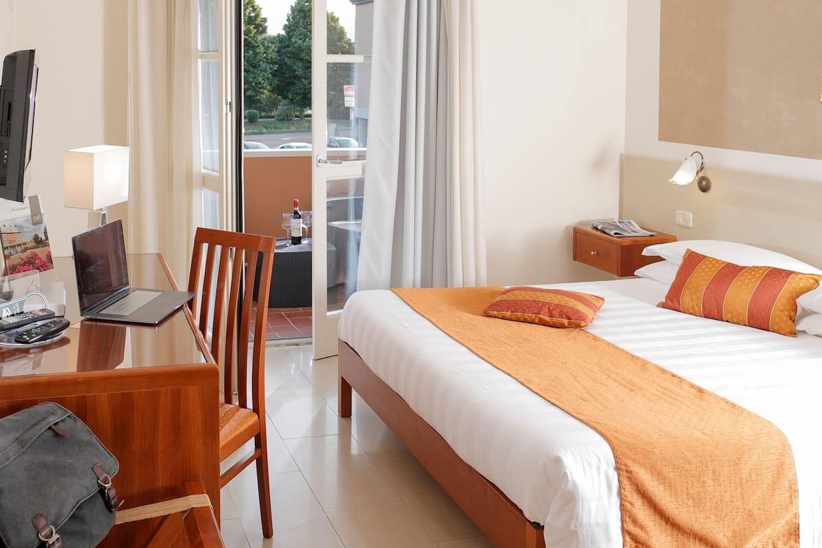 Una camera d'albergo con un letto, una scrivania con un portatile, una sedia, un comodino e vista dalla finestra.
