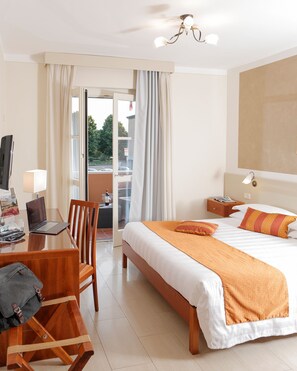 A hotel room with a bed, a desk with a laptop, a chair, a nightstand, and a view through the window. - Hotel Michelangelo (Terranuova Bracciolini)