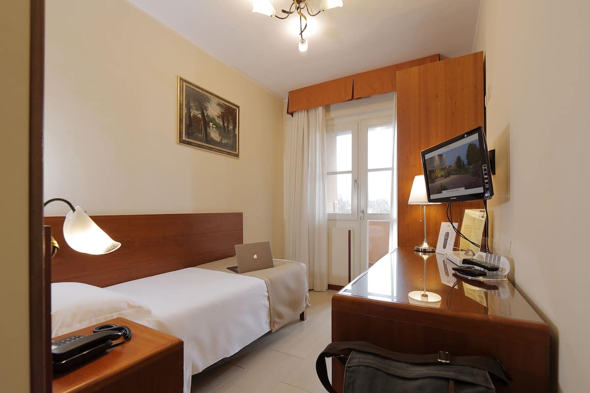 Una camera d'albergo con un letto, una scrivania con un computer, una televisione e un telefono sul comodino.