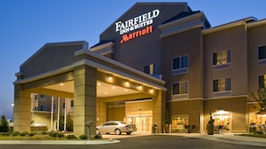 Un hotel Fairfield Inn & Suites Marriott con un acceso cubierto, un coche estacionado frente a él y una fachada bien iluminada.