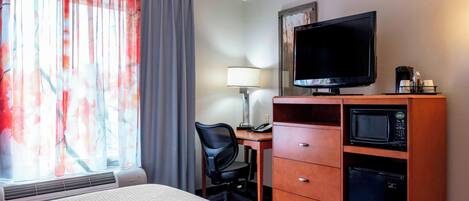 Habitación de hotel con cama, escritorio con silla, televisión, microondas y cafetera.