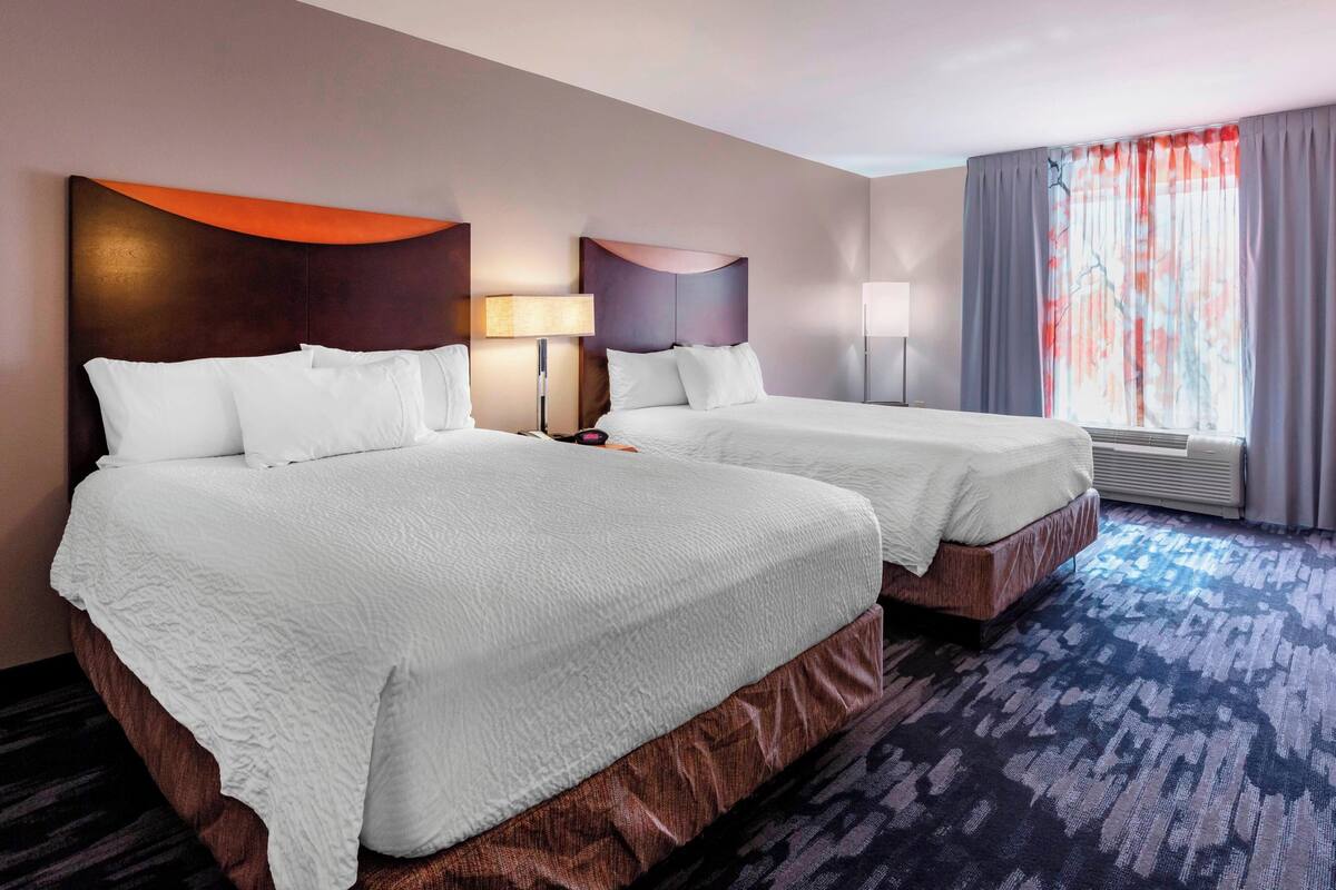 A hotel room with two beds, a large window with curtains, and a patterned carpet.