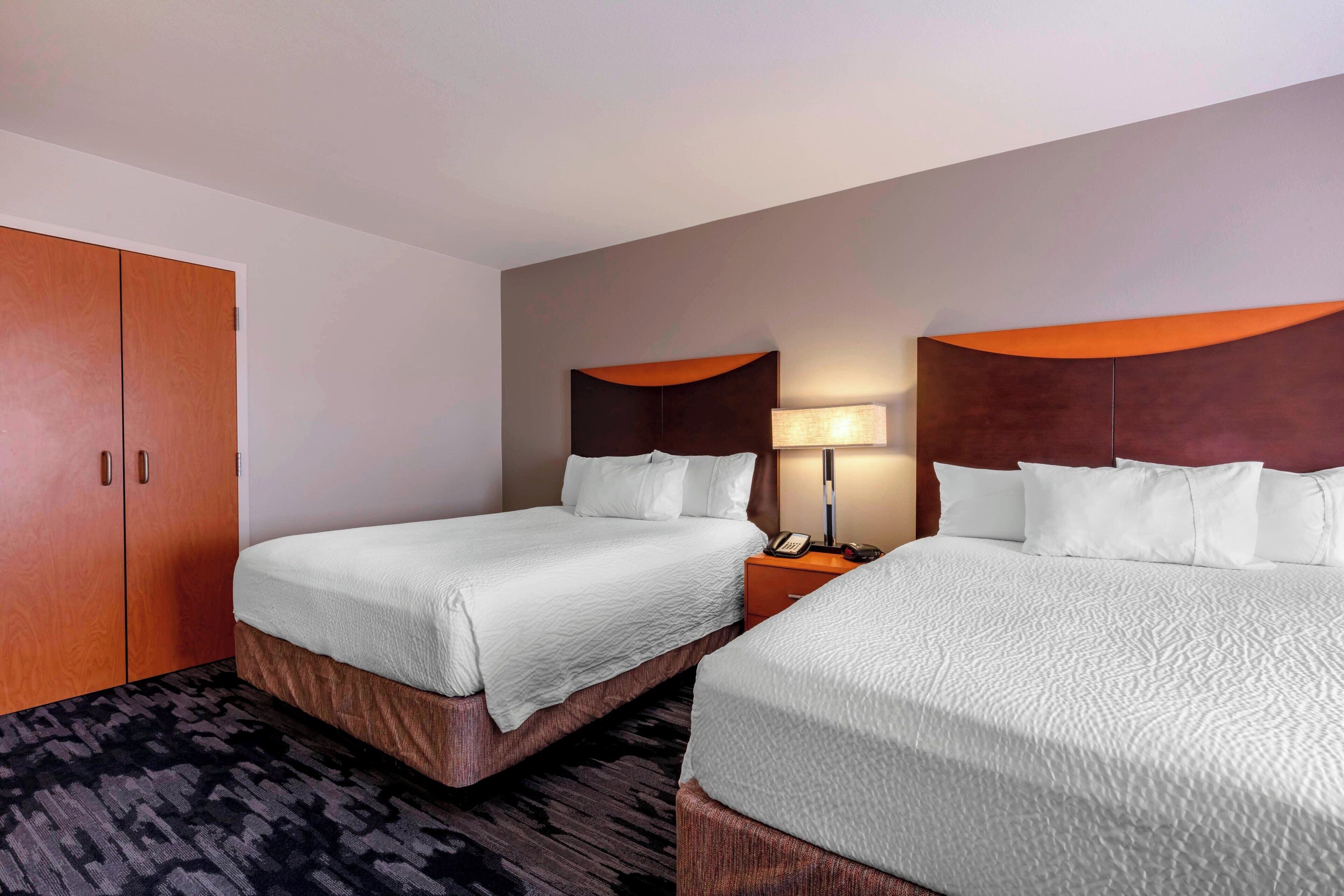 A hotel room with two beds, a wardrobe, a nightstand, and a lamp.