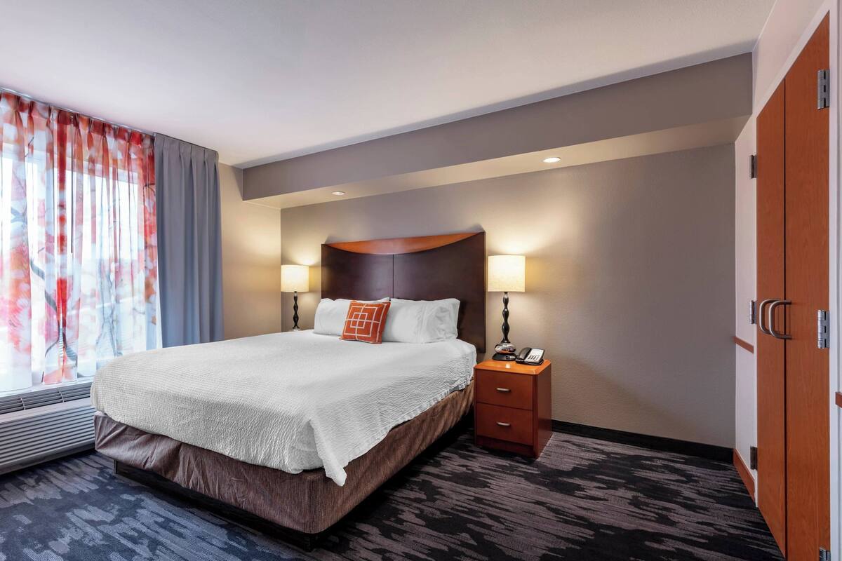 A hotel room with a large bed, two bedside tables with lamps, a telephone, and a wardrobe.