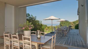 Una terraza de madera con mobiliario exterior, incluyendo una mesa y sillas, y dos sombrillas que dan sombra.