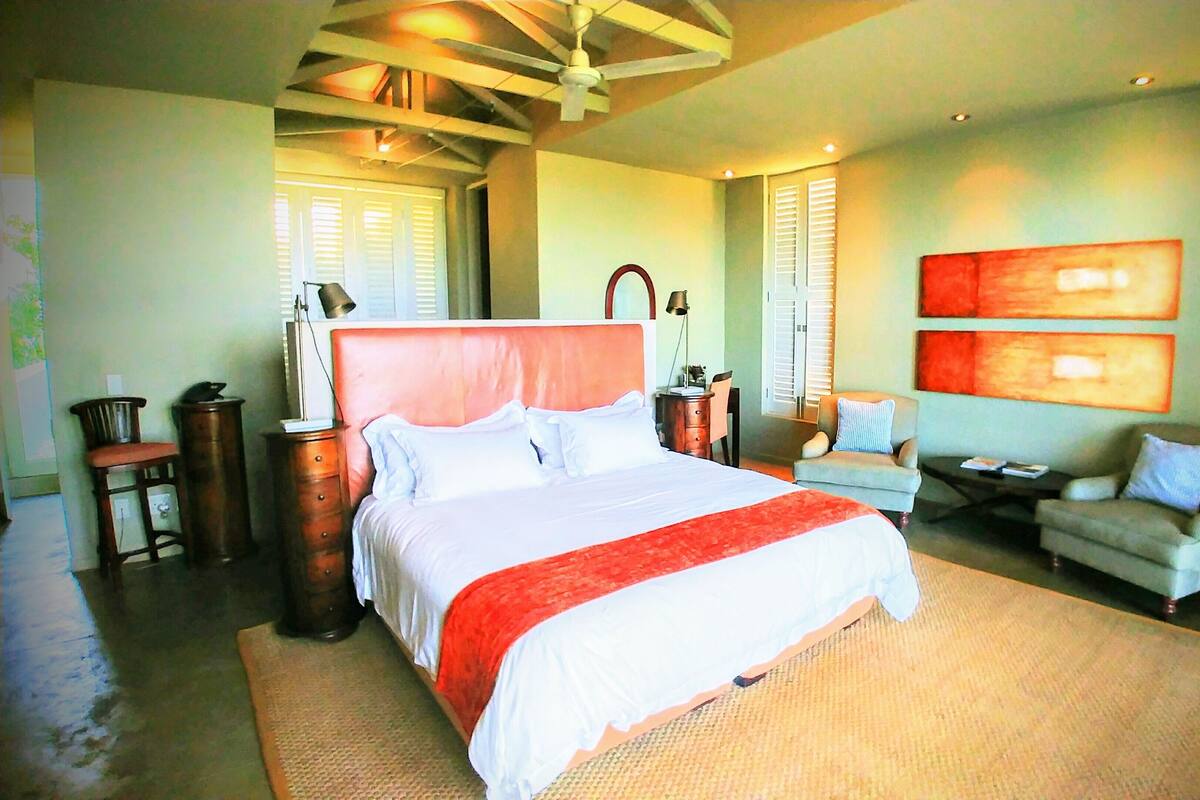 A spacious bedroom with a large bed, a desk, a chair, and a sofa.