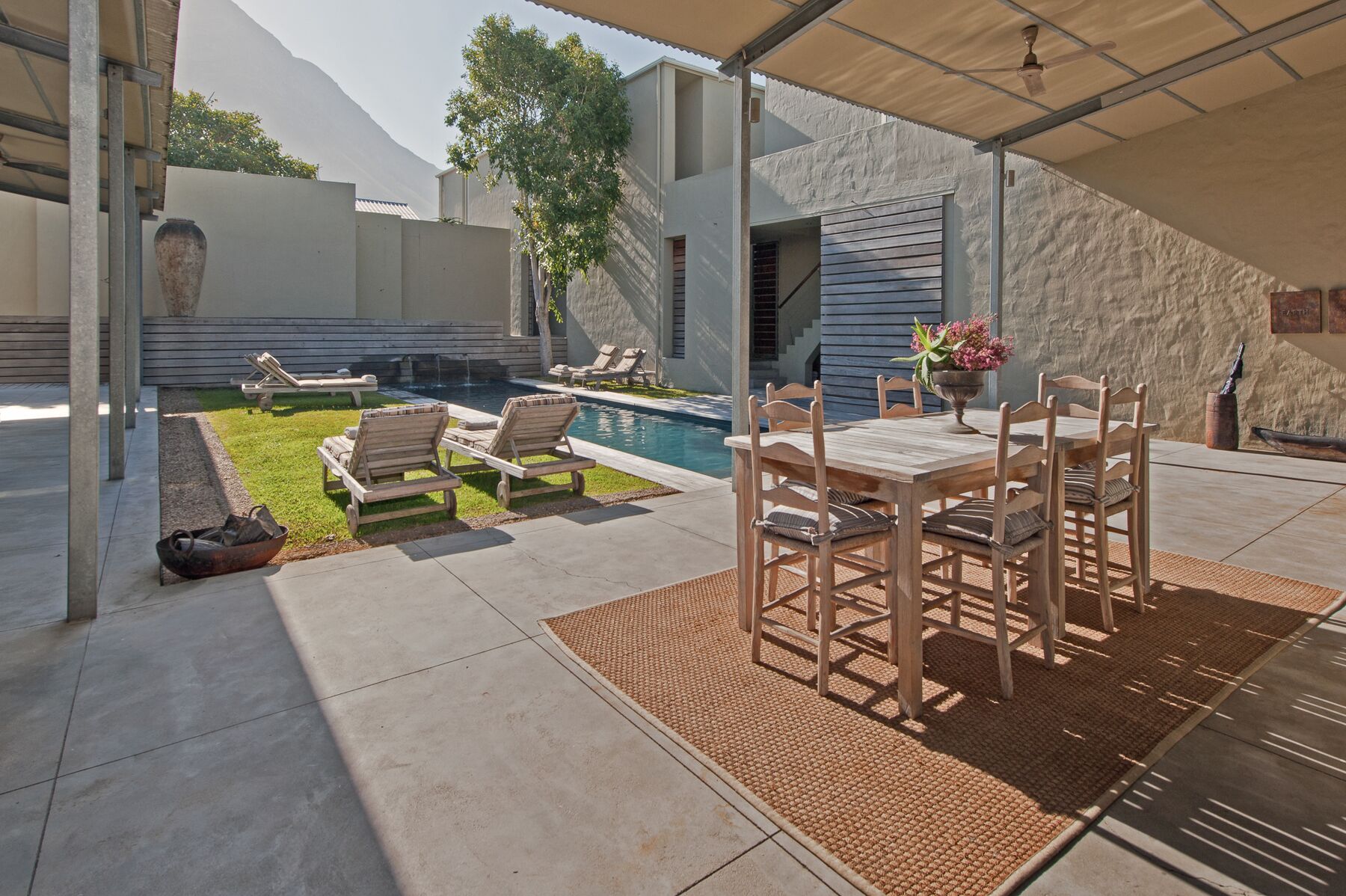 An outdoor patio with a pool, lounge chairs, and a dining table.