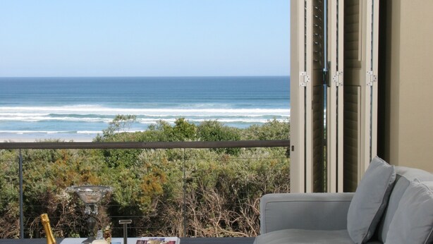 A balcony with a view of the ocean, a grey sofa, and a table with a bottle and glasses.