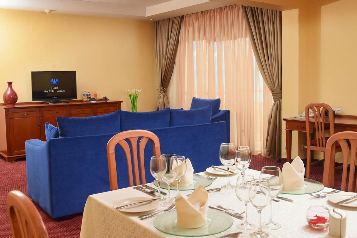 Un área de comedor con una mesa preparada para cuatro personas, un sofá azul y un televisor al fondo.