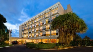 Un hotel de varios pisos con un diseño moderno, que cuenta con balcones en cada planta, una entrada bien iluminada y un exuberante paisaje.