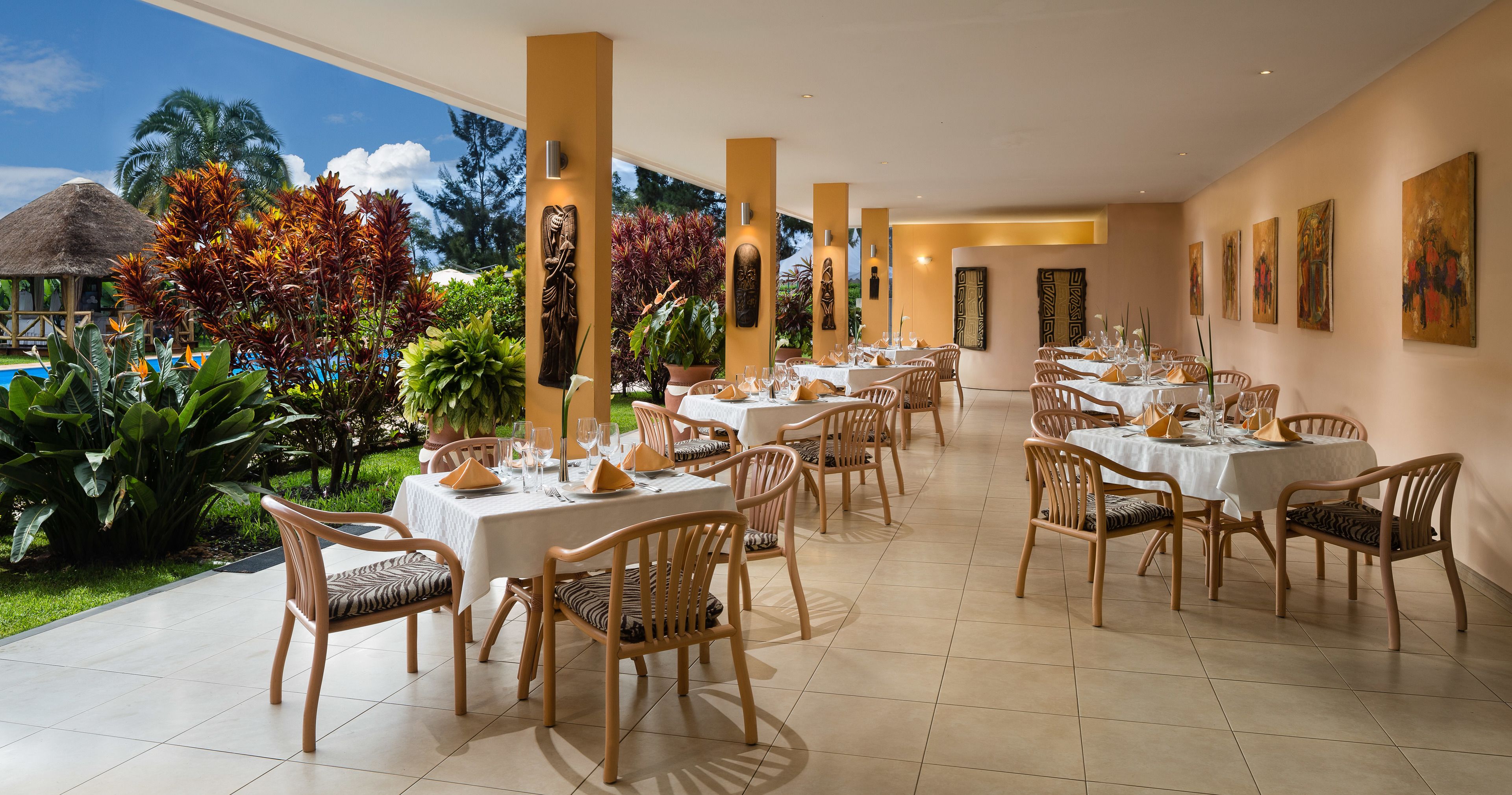 A restaurant with multiple tables and chairs, surrounded by tropical plants and a pool.