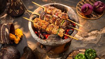 Montaje de cocina tradicional con brochetas de carne y verduras sobre fuego abierto, rodeado de diversos utensilios y alimentos.