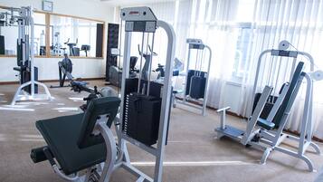 Ein Fitnessstudio mit verschiedenen Trainingsgeräten, einem großen Spiegel und einer Uhr an der Wand.