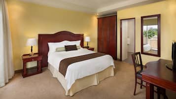 Une chambre d’hôtel avec un grand lit, deux tables de chevet avec des lampes, une armoire en bois, un bureau avec une chaise et un miroir.